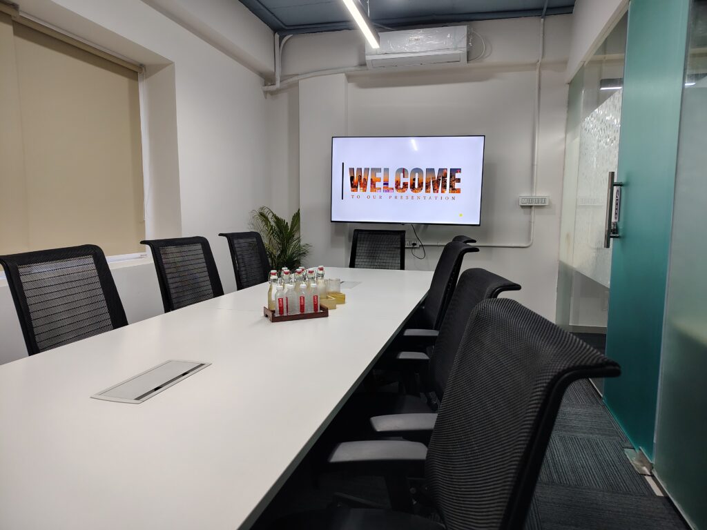 A modern meeting room at Elite Co-Works in BTM Layout, Bangalore, equipped with a wall-mounted big monitor, air conditioning, and ergonomic seating, designed to support productive team discussions and presentations in a premium coworking space environment.