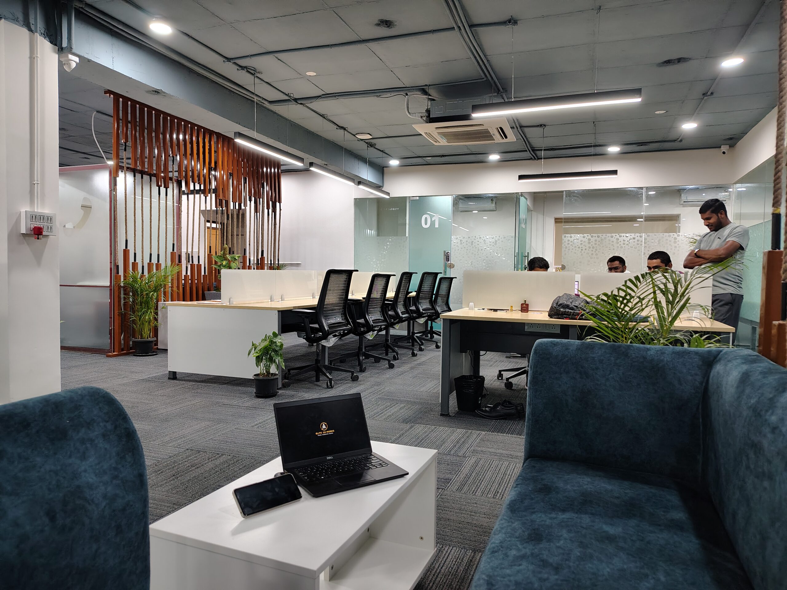 A spacious and well-designed office area at Elite Co-Works in BTM Layout, Bangalore, featuring organized work tables with comfortable seating, stylish sofa furniture for informal meetings, and refreshing indoor plants that enhance the aesthetic and provide a calming work environment — ideal for startups, freelancers, and growing teams seeking a flexible coworking space.